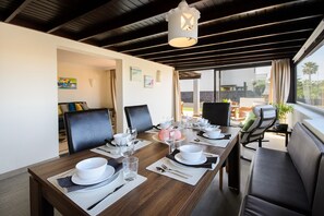 A dining area with a long table set for four, two chairs on each side, a sofa, and a window with a view of the outdoors.