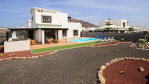 Una casa moderna de dos pisos con piscina, mobiliario exterior y jardín ajardinado.