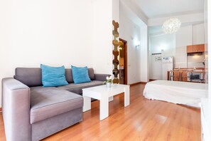 A modern living room with a grey sofa, white coffee table, and a bed with a white duvet.