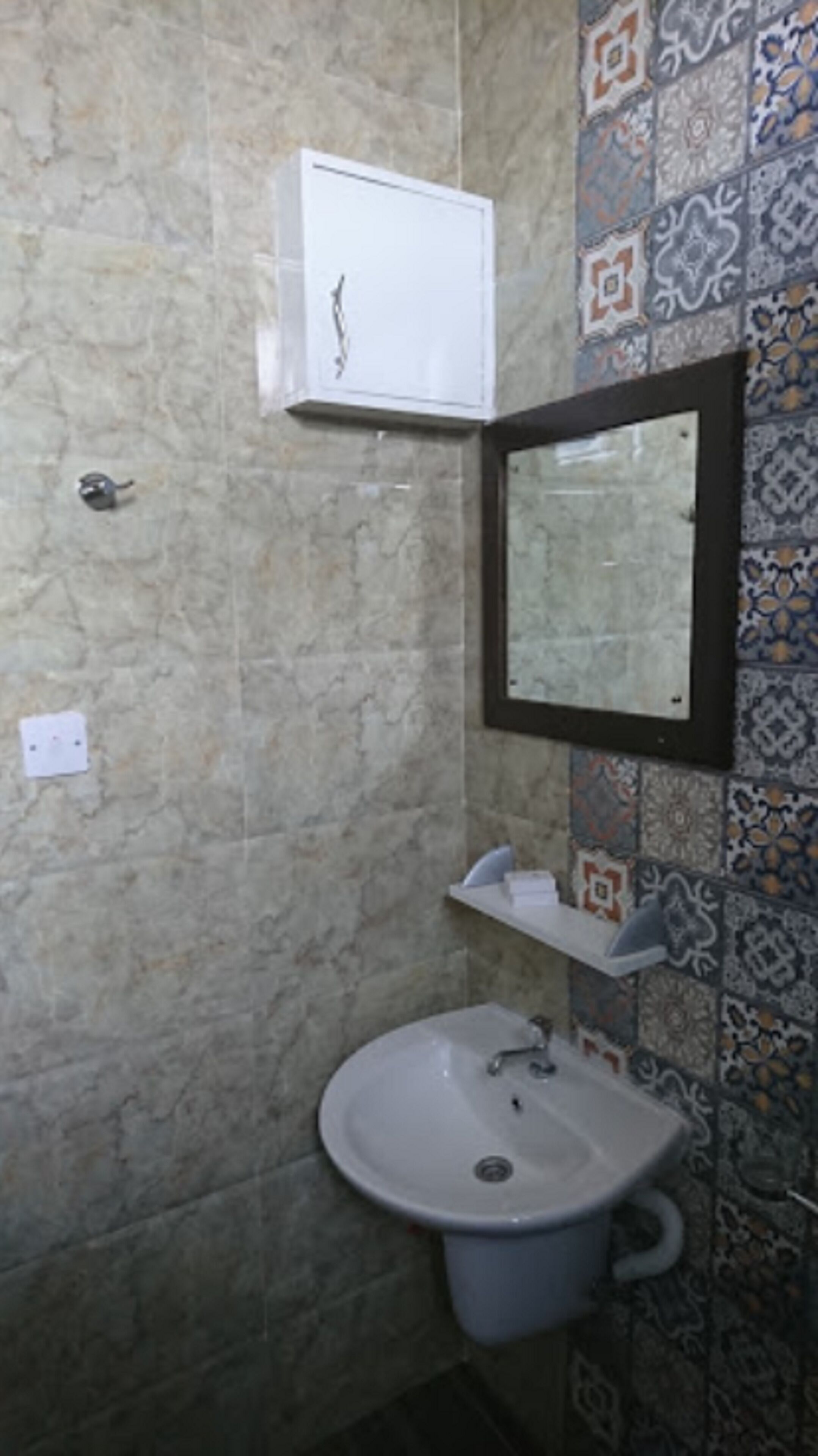 A bathroom with a marble wall, a sink, a mirror, and a tiled backsplash.