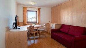 Ein Zimmer mit einem Holztisch, einem roten Sofa, einem Fenster mit Vorhängen und Blick auf Häuser.