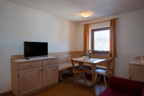 A small room with a wooden desk, a television, a window with curtains, and a red sofa.