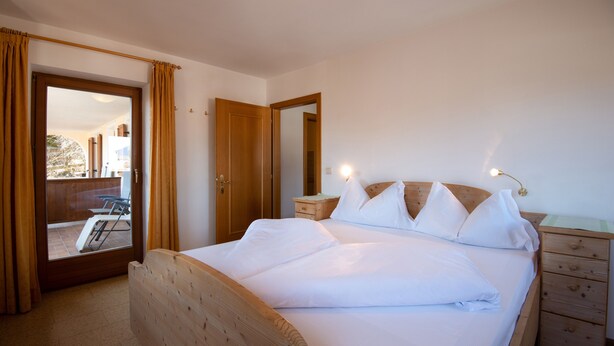 Ein Schlafzimmer mit einem hölzernen Bett, einem Nachttisch, einem Spiegel und einer Schiebetür, die zu einem Außenbereich führt.