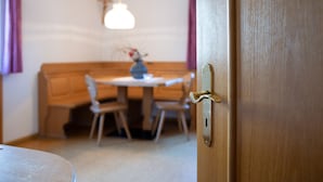 A wooden door with a brass handle, a round table with chairs, and a cross on the wall.
