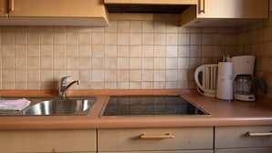 A kitchen with wooden cabinets, a stainless steel sink, a built-in stovetop, and a coffee maker.