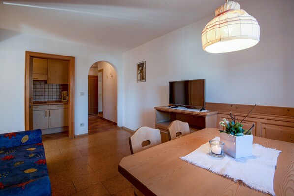 A room with a wooden dining table, a TV, a small white cabinet, and a sofa with a floral pattern.
