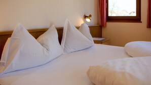 Een hotelkamer met een net opgemaakt bed, een nachtkastje, een lamp en een raam met gordijnen.