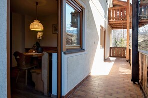 Un espace extérieur abrité, doté d’une rambarde en bois, d’un sol carrelé et d’une fenêtre offrant une vue sur les arbres et les montagnes.