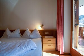 Une chambre à coucher avec un lit, des oreillers, une table de chevet, un tiroir et une fenêtre avec des rideaux.