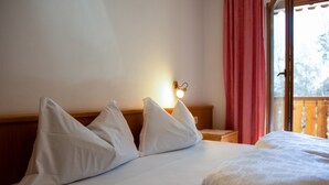 A hotel room with a bed, pillows, a nightstand, a lamp, and a window with curtains. - Comfortable Apartment 3 "Zur Sonne" with Mountain View, Garden & Wi-Fi (Lajen)