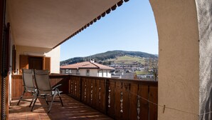 A balcony with two chairs, a view of a hilly landscape, and a building with a red roof in the background. - Comfortable Apartment 3 "Zur Sonne" with Mountain View, Garden & Wi-Fi (Lajen)