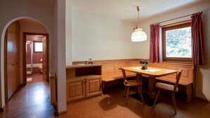 A kitchen with a dining table, chairs, a hanging light fixture, and a window with curtains. - Comfortable Apartment 3 "Zur Sonne" with Mountain View, Garden & Wi-Fi (Lajen)