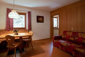 Un coin repas avec une table en bois, des chaises, un luminaire suspendu et un canapé rouge à motifs.