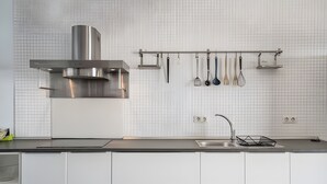 Een moderne keuken met witte kasten, een roestvrijstalen afzuigkap en een keukengerei rek.