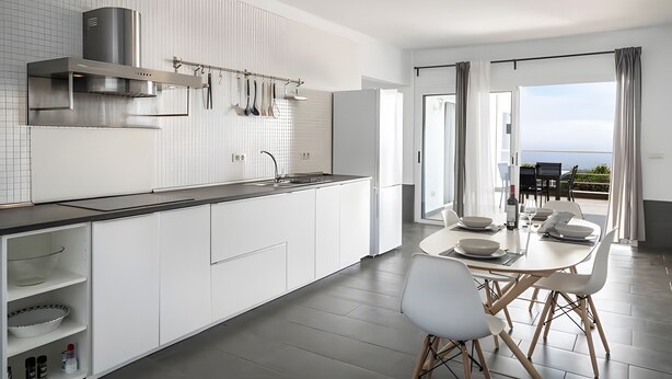 Een moderne keuken met witte kasten, roestvrijstalen apparatuur en een eethoek met een tafel en stoelen.