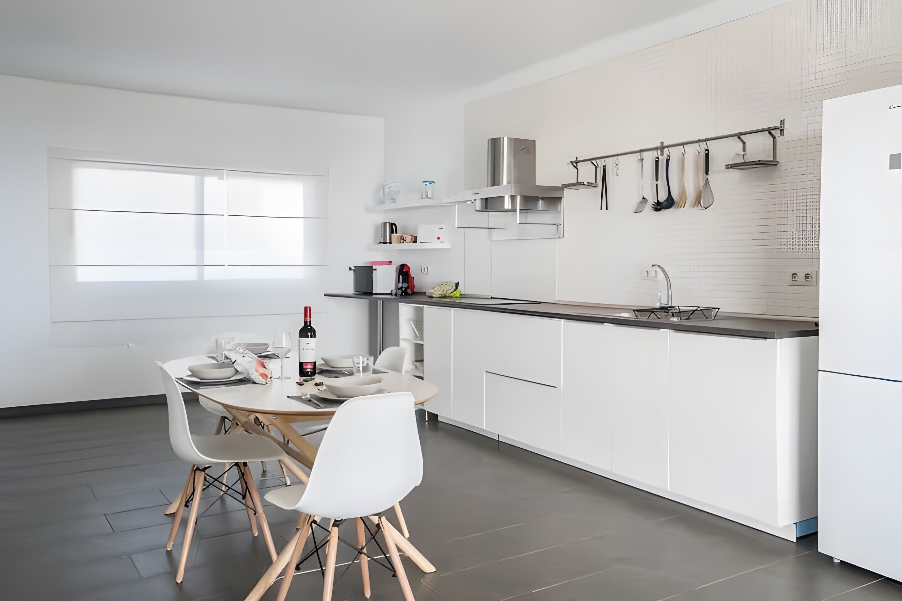 A modern kitchen with white cabinetry, a dining area with a table and chairs, and a window providing natural light.