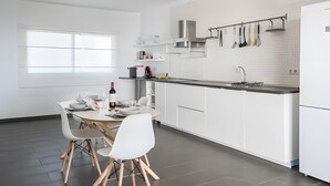 Een moderne keuken met witte kasten, een eethoek met tafel en stoelen, en een raam dat natuurlijk licht biedt.