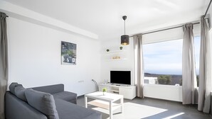 Een moderne woonkamer met een grijze bank, een witte salontafel, een flatscreentelevisie en een balkon met gordijnen.