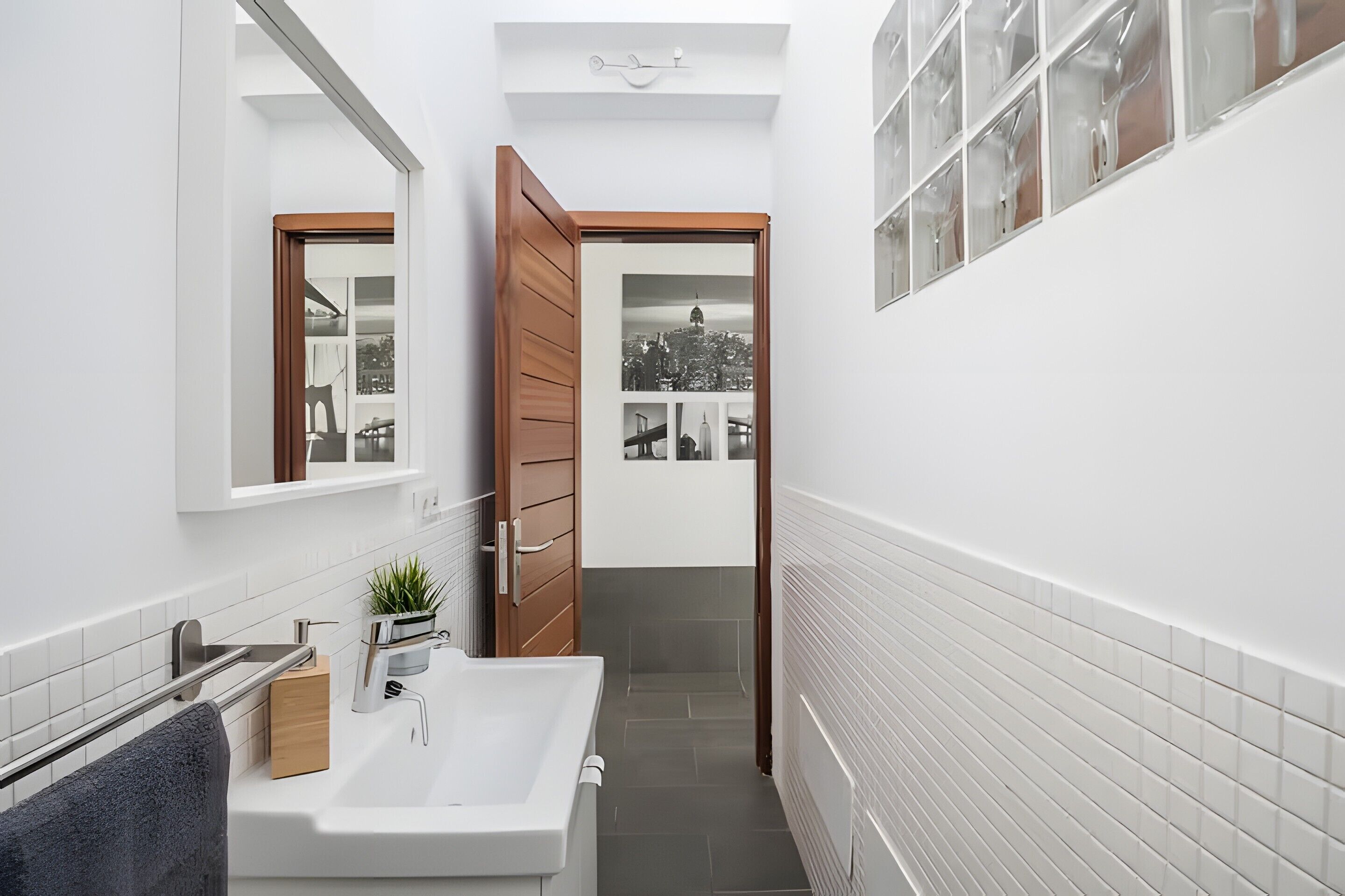 A narrow bathroom with a white sink, wooden door, and a small window.
