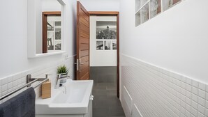 Een smalle badkamer met een wit wastafelmeubel, houten deur en een klein raam.
