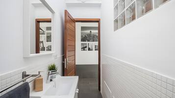 A narrow bathroom with a white sink, wooden door, and a small window.