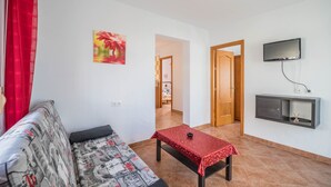 A living room with a sofa, a small table, a TV, and a door leading to another room. - Rural Home "La Ermita" with Pool, Terrace, Wi-Fi & Air Conditioning (Conil de la Frontera)