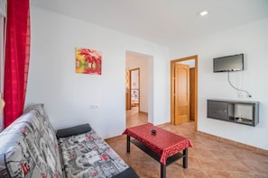 A living room with a sofa, a small table, a TV, and a door leading to another room.