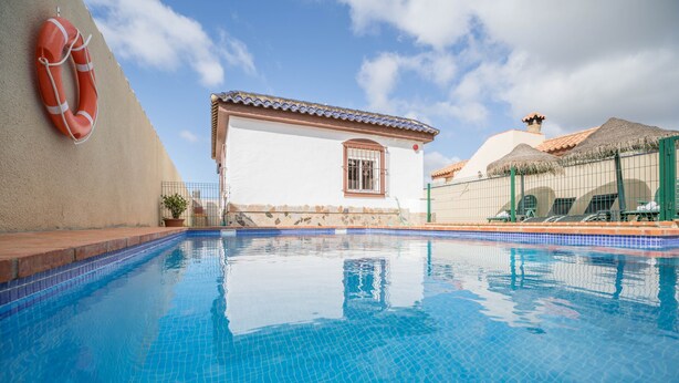 A swimming pool with a lifebuoy, a small building with a window, and a thatched roof structure. - Rural Home "La Ermita" with Pool, Terrace, Wi-Fi & Air Conditioning (Conil de la Frontera)