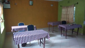 A room with four tables covered with striped tablecloths, a clock on the wall, and a window with curtains.