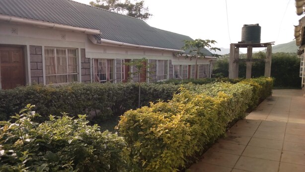 A building with a tiled roof, a water tank on a wooden stand, and a well-maintained hedge along a paved walkway.