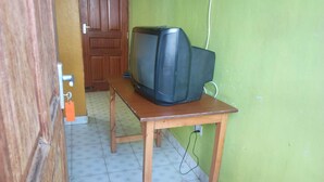 A small room with a wooden table, a television on top, and a door in the background.