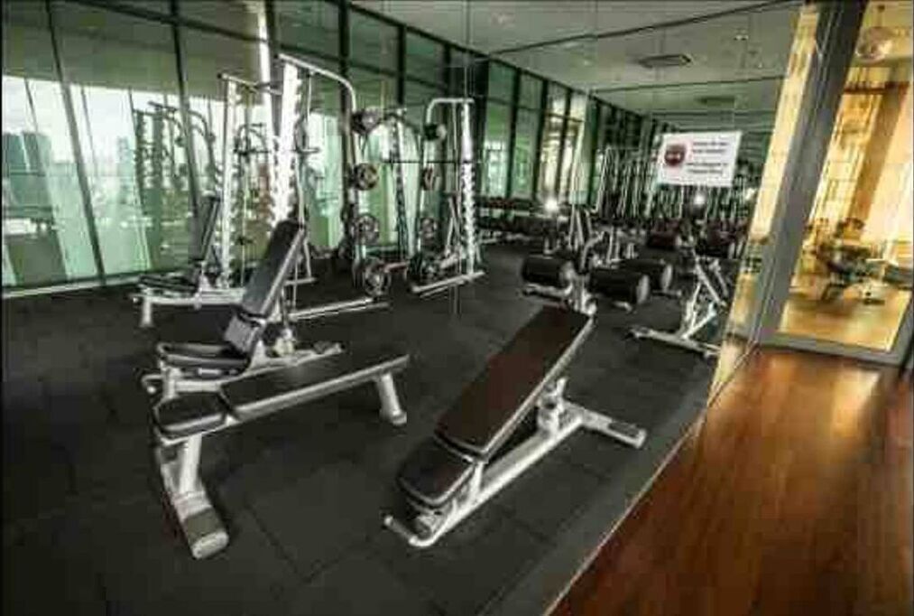 Une salle de sport équipée de divers appareils d’exercice, dotée de grandes fenêtres et présentant un design moderne et épuré.