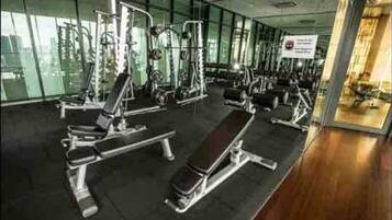 Une salle de sport équipée de divers appareils d’exercice, dotée de grandes fenêtres et présentant un design moderne et épuré.