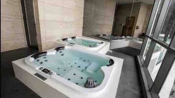 Un espace spa moderne doté de deux bains à remous et d’une douche séparée par des parois en verre.