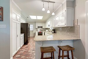 A kitchen with white cabinets, a granite countertop, and a brick-patterned floor.