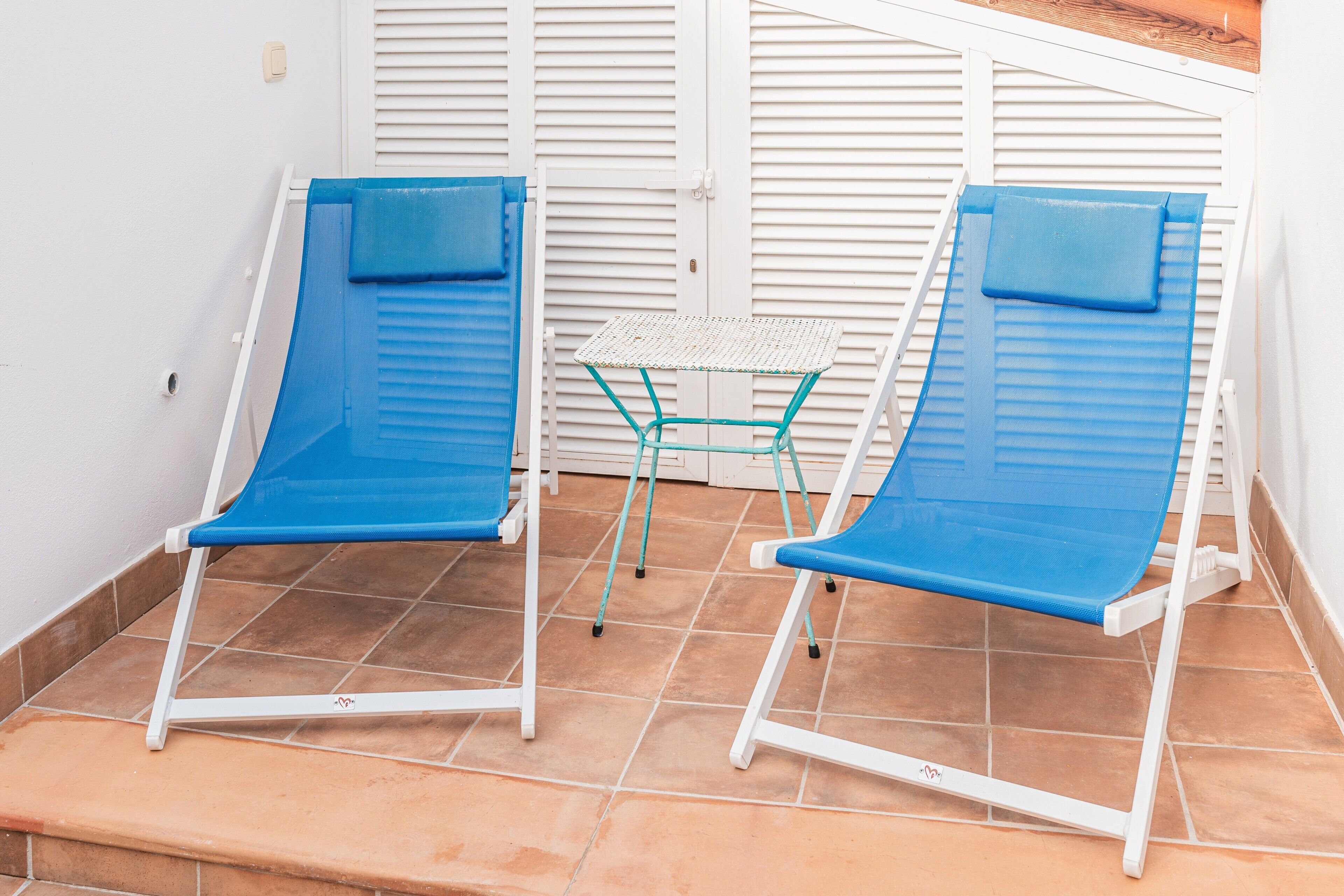 Dos sillones azules con estructura blanca en un patio con baldosas.
