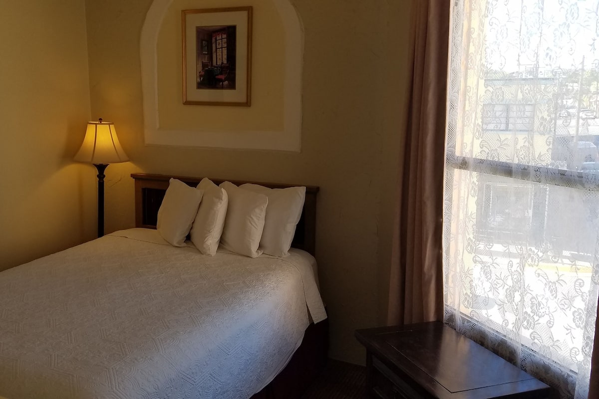 A neatly made bed with a white duvet and pillows, a bedside lamp, and a framed picture on the wall.