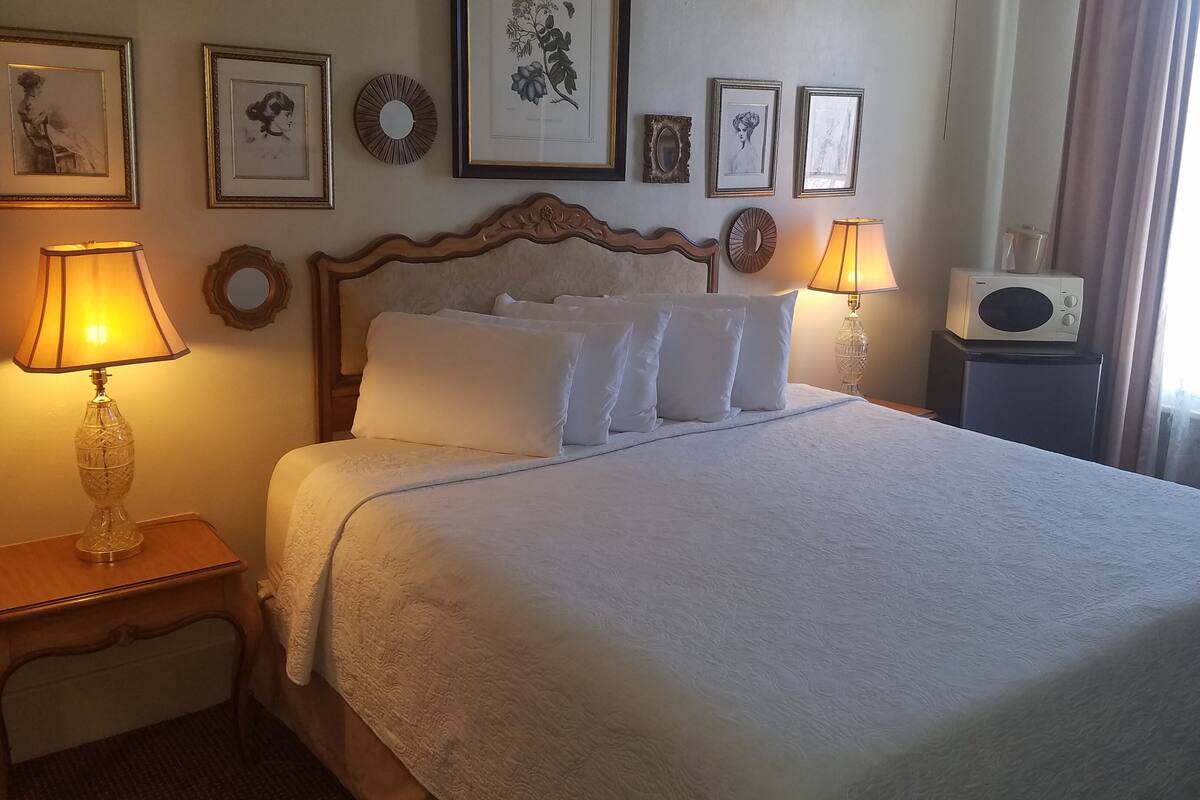 A neatly made bed with white linens, two bedside lamps, and a wall adorned with framed pictures.