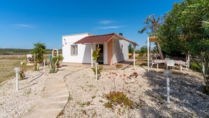 Una casetta con tetto in tegole, un vialetto lastricato e un giardino con diverse piante.