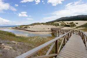 A wooden boardwalk leading to a beach with dunes and a hill in the background.
