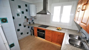 A kitchen with white tiles, a stove, oven, sink, and wooden cabinets.