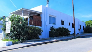 A white building with a covered porch, a brick section, and a signboard.
