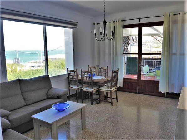 A room with a sofa, dining table, chairs, a bowl, and a view through a large window.