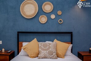 A bedroom with a blue wall, a bed with two pillows, and a nightstand with a remote control and a candle.