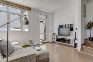 Ein modernes Wohnzimmer mit einer Couch, einem Glastisch, einer Stehlampe, einem Fernseher und einer Treppe.