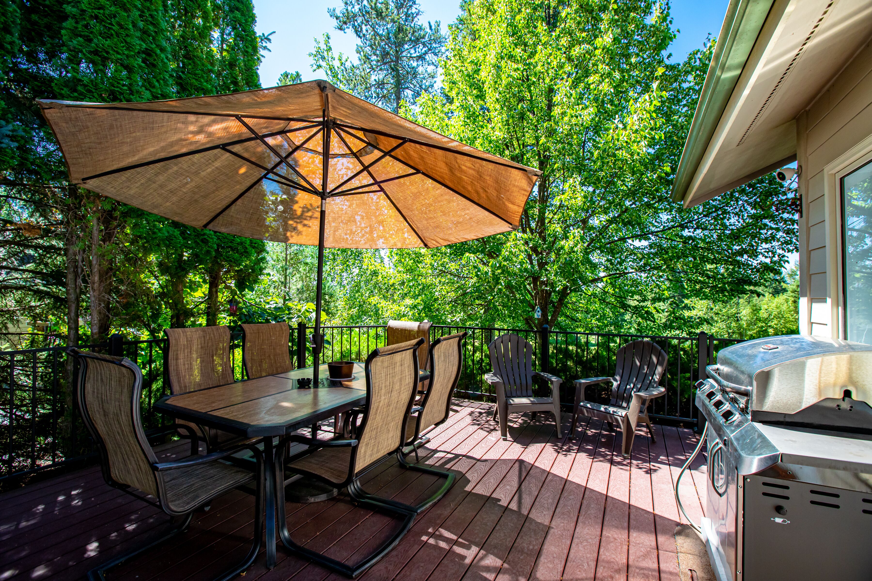 Eine Terrasse mit Tisch, Stühlen, einem Grill und einem großen Sonnenschirm.