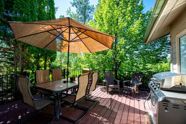 A deck with a table, chairs, a grill, and a large umbrella.