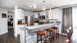 A modern kitchen with white cabinets, a granite countertop, stainless steel appliances, and a bar area with stools. - Town Home with Hot Tub, Sleeps 6 in Meadow Lake Resort and Golf Course (Columbia Falls)