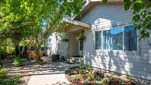 A house with a covered porch, a small outdoor seating area, and a landscaped garden with mulch and plants. - Town Home with Hot Tub, Sleeps 6 in Meadow Lake Resort and Golf Course (Columbia Falls)