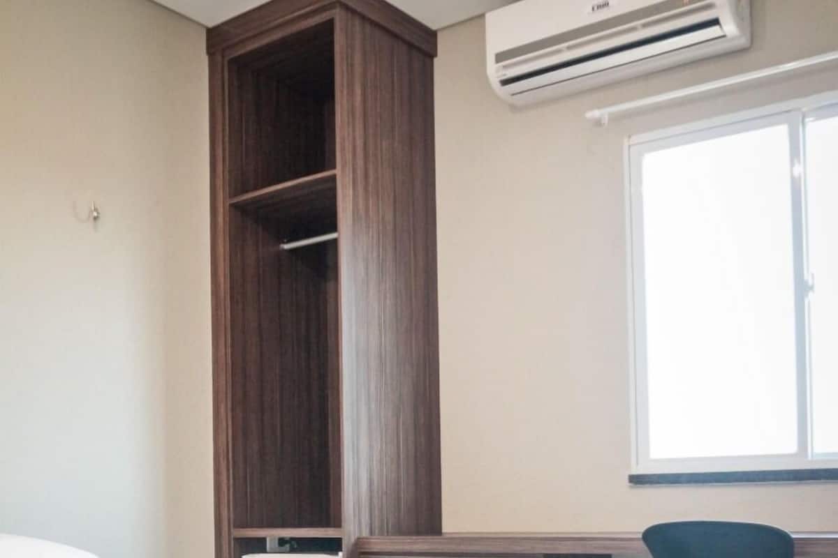 Una habitación de hotel con cama, escritorio, silla, armario y aire acondicionado.
